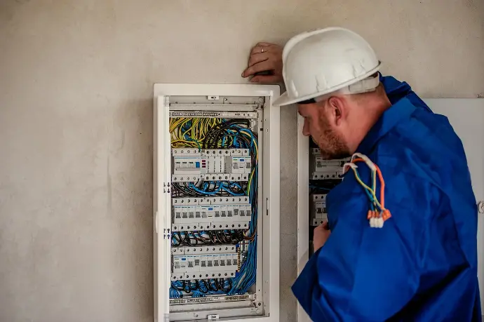 Elektriker bei Schaltschrank-Wartung | Professionelle Gebäudetechnik Elektriker überprüft Schaltschrank mit sauber organisiertem Kabelmanagement, Fokus auf Sicherheit und Effizienz in der Elektrotechnik.