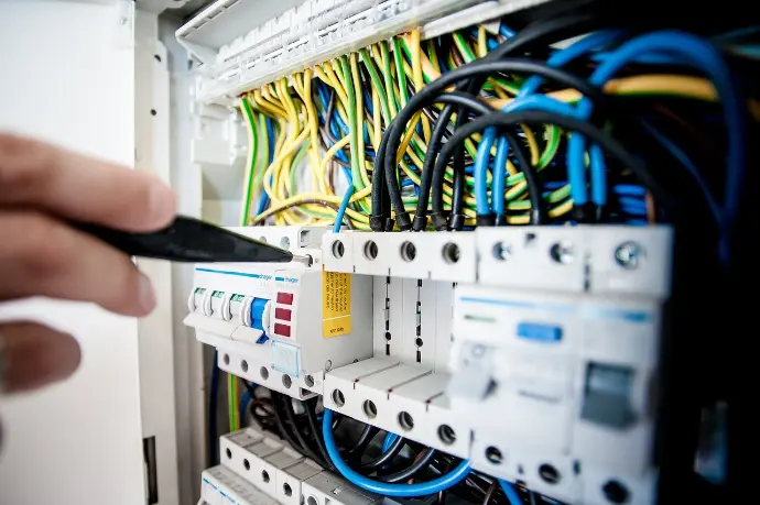 Schaltschrank und Kabelmanagement | Effiziente Elektrotechnik-Lösungen Elektriker im blauen Overall führt Inspektion und Wartung an einem geöffneten Schaltschrank durch, Fokus auf professionelle Gebäudetechnik.